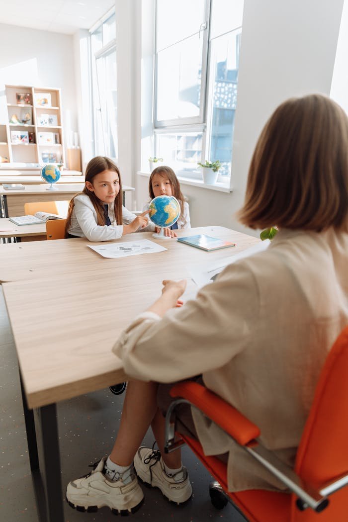Mastering the First Impression: Your intriguing post title goes here Two children in a bright classroom discussing geography with their teacher.